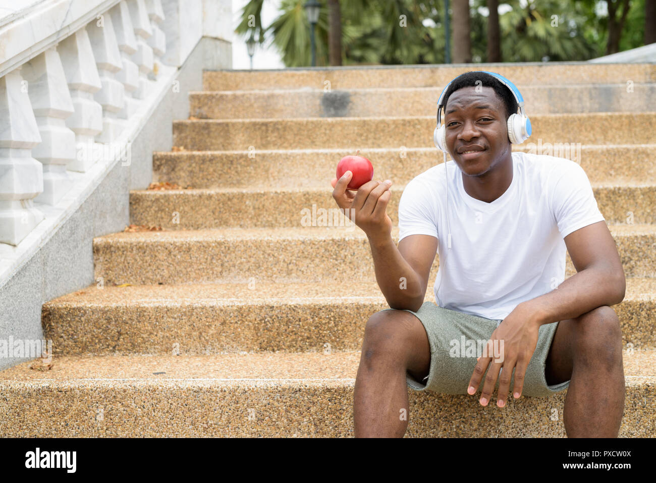 Afrikanischer Mann Musik hören mit Kopfhörern und holding red apple Stockfoto