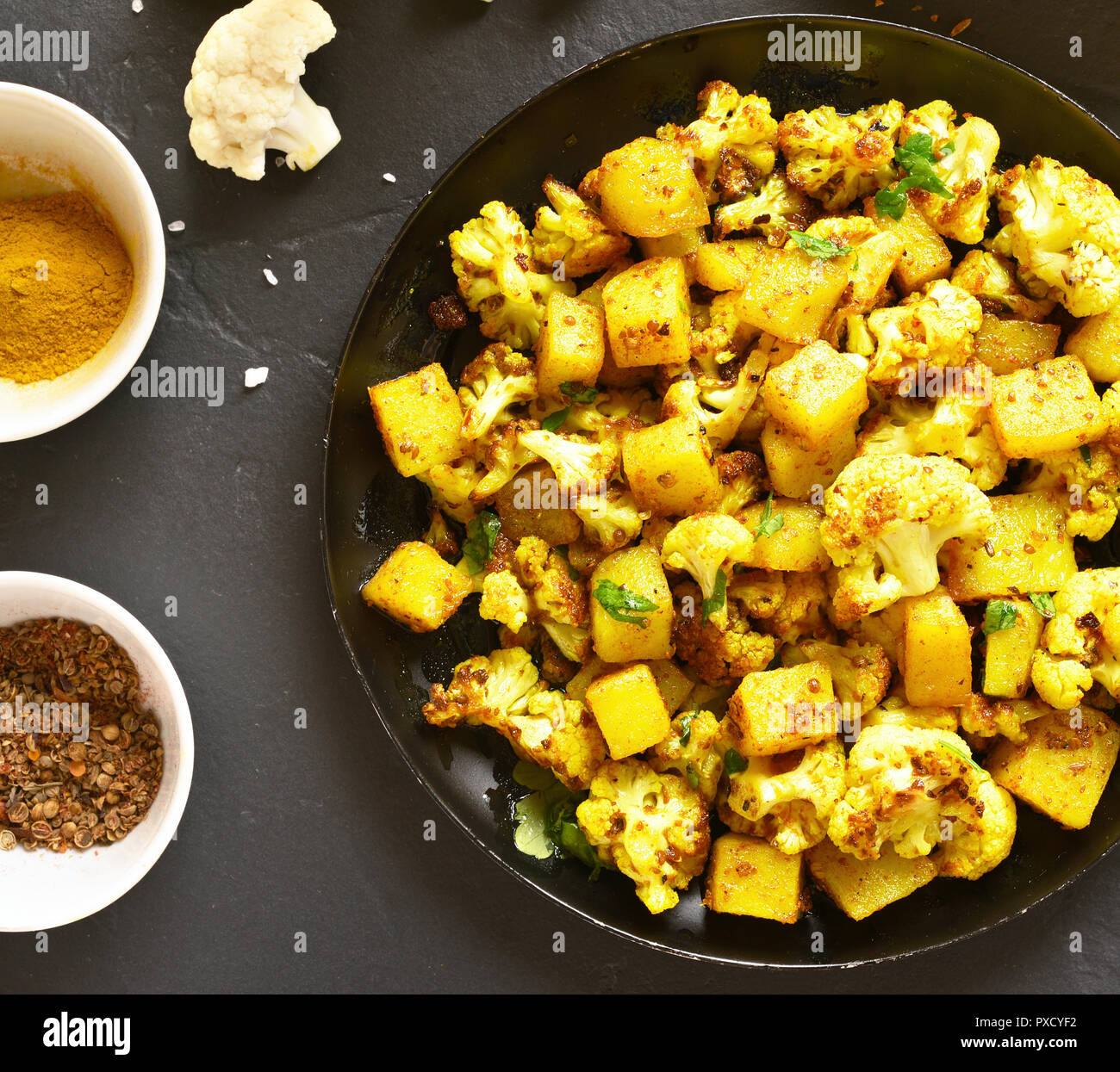Nahaufnahme von Aloo Gobi indische Gericht. Gebratener Blumenkohl mit Kartoffeln auf schwarzen Stein Hintergrund. Ansicht von oben Stockfoto