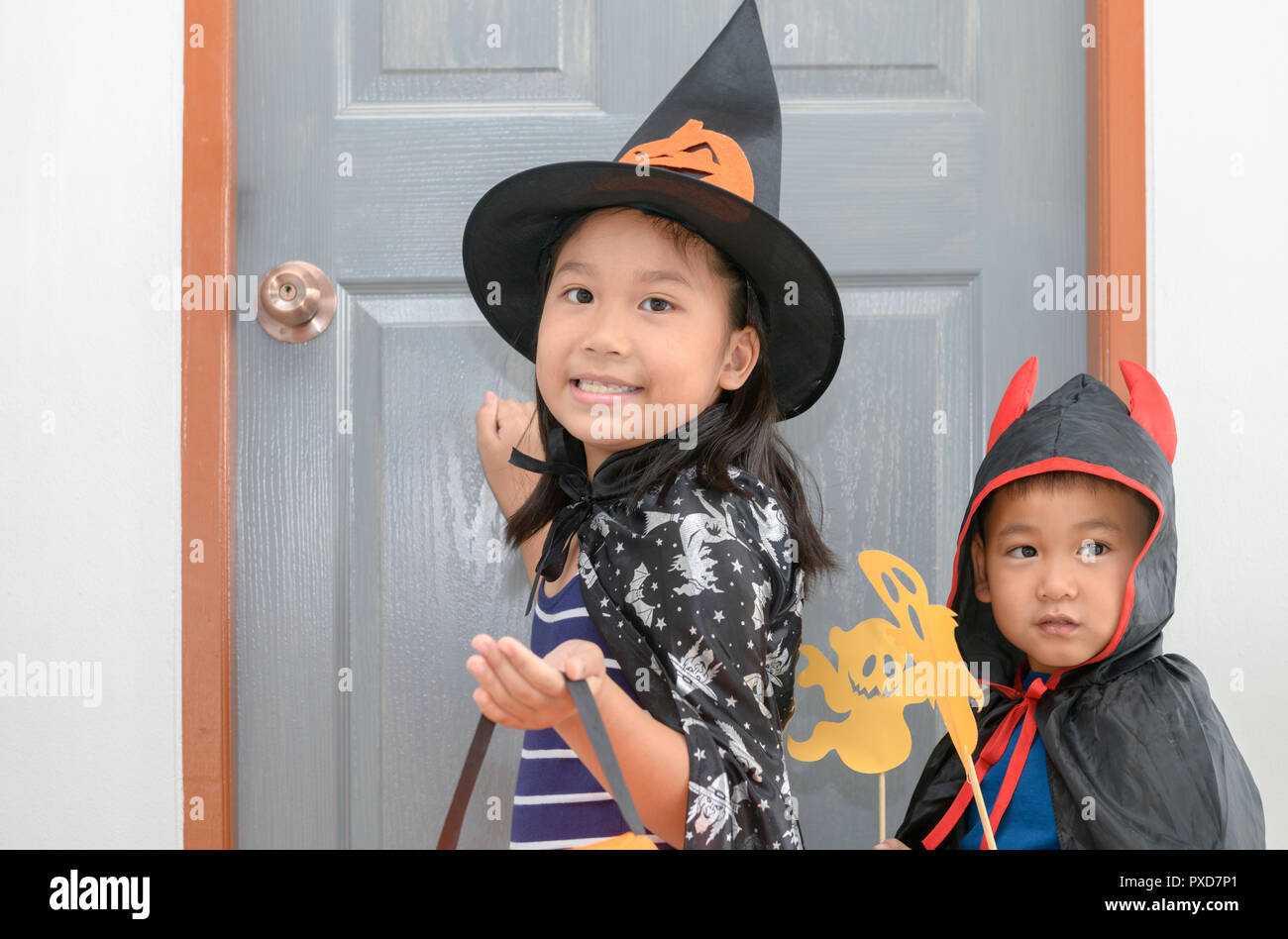 Süße Mädchen tragen Hexen klopfen an die Tür mit kleinen Jungen Teufel, Halloween Konzept Stockfoto