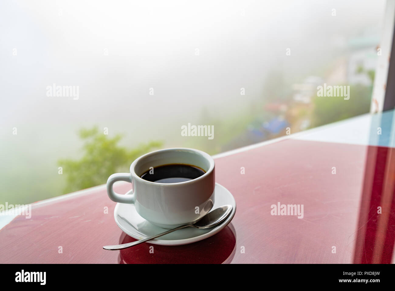 Schwarzen Kaffee in weißen Schale, die durch die Fenster Hintergrund der Berge Nebel und Dunst auf Wald am Morgen. Fühlt sich gut an. Stockfoto