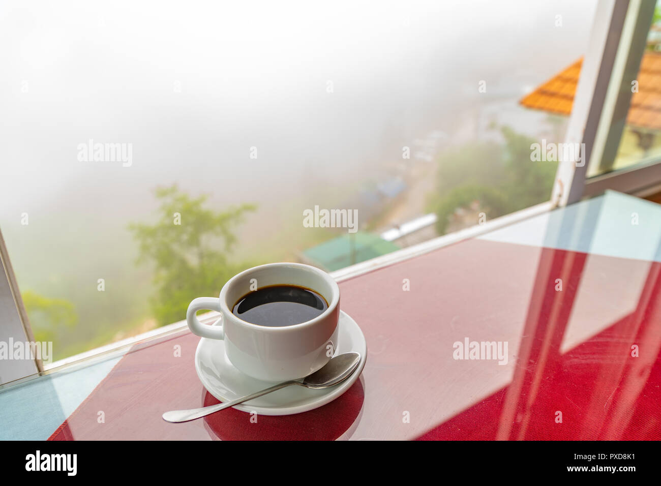 Schwarzen Kaffee in weißen Schale, die durch die Fenster Hintergrund der Berge Nebel und Dunst auf Wald am Morgen. Fühlt sich gut an. Stockfoto