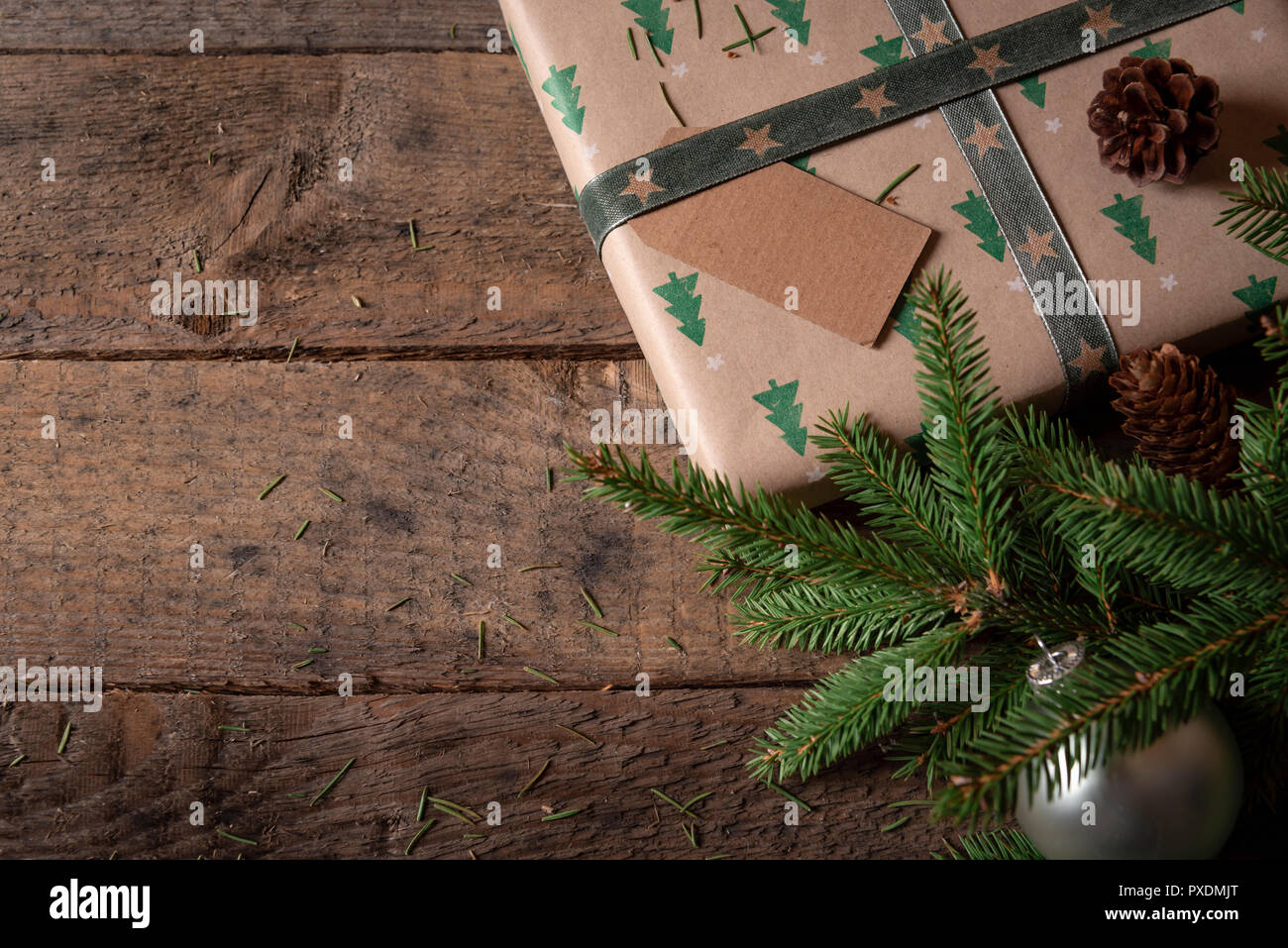 Weihnachten Grußkarte mit einem braunen Geschenk mit Weihnachtsbäumen Design, ein ungeschriebenes Tag und Grüne Tanne Zweige auf einem rustikalen Holztisch. Stockfoto