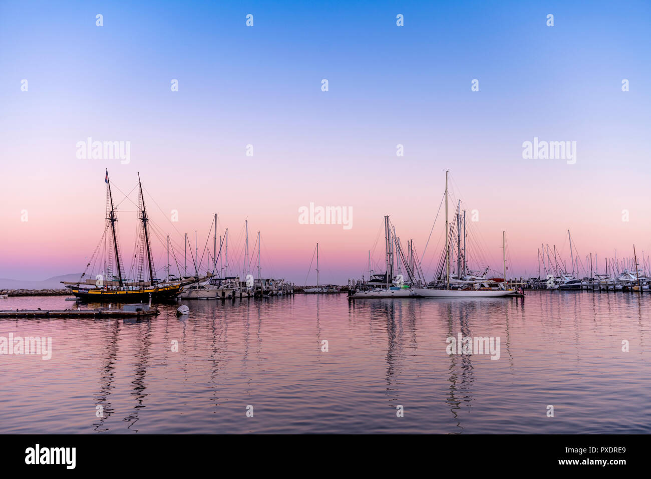 Als die Sonne sinkt, ein rosa Inversionsschicht Formen hinter der Bucht von Segelbooten, Framing eine maritime klassische Bild. Stockfoto