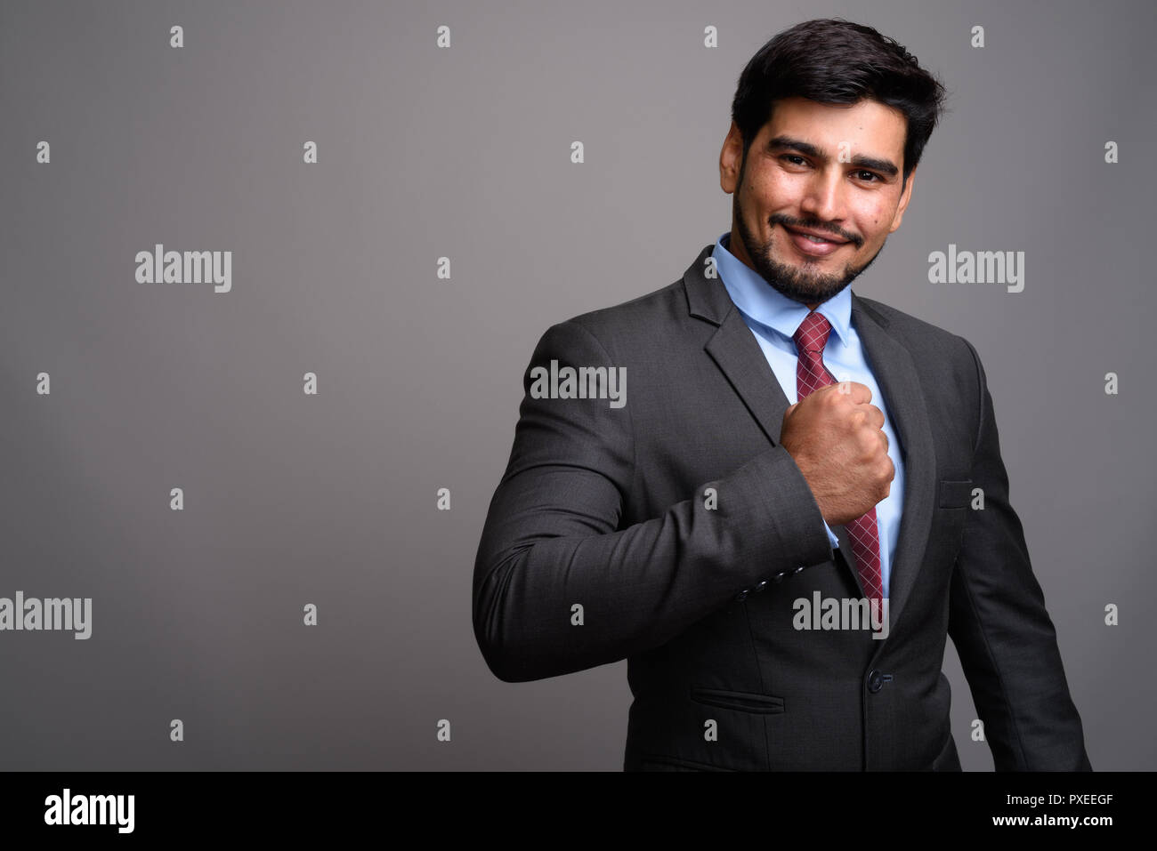 Die Jungen gut aussehenden bärtigen Persischen Geschäftsmann gegen Grau backgrou Stockfoto