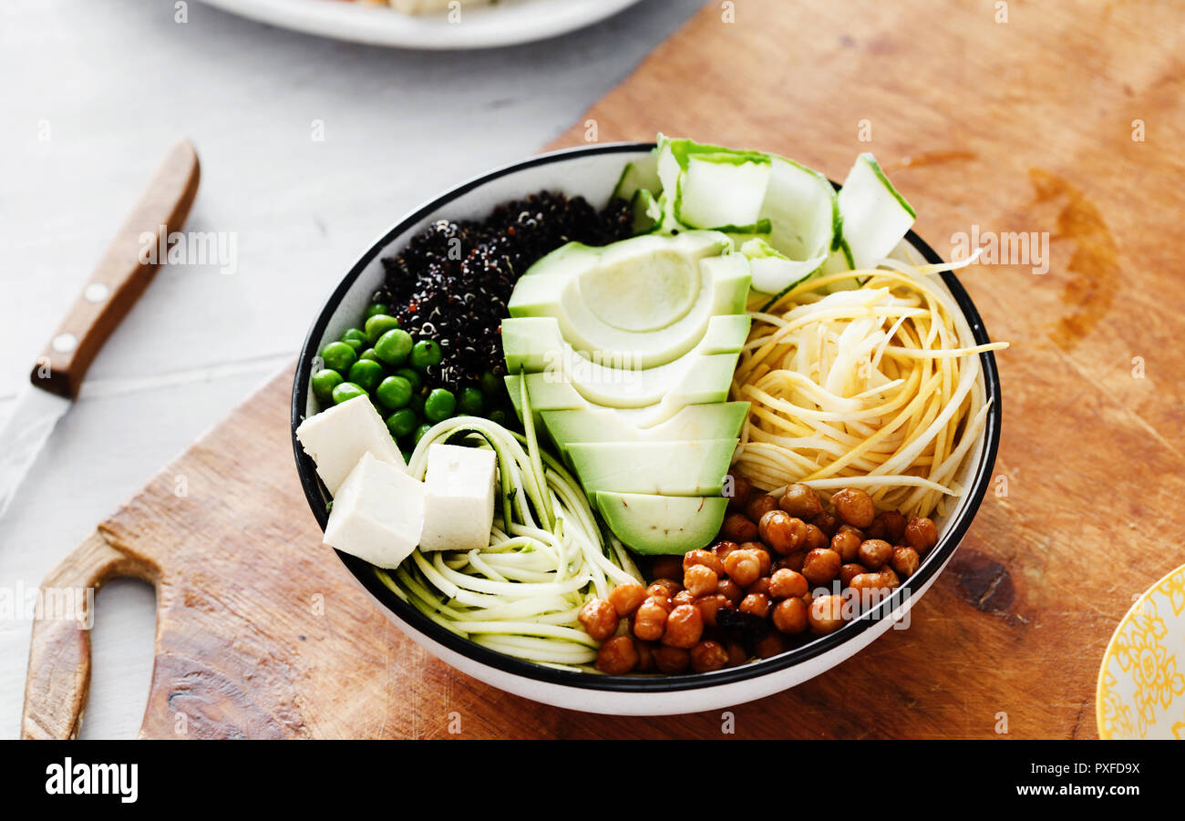 Ansicht von oben Buddha Schüssel auf weiße Holztisch. Sauber und gesund Gesunde Ernährung Konzept. Avocado, Erbsen, Quinoa, Gurken, Zucchini, Kichererbsen und Spi Stockfoto