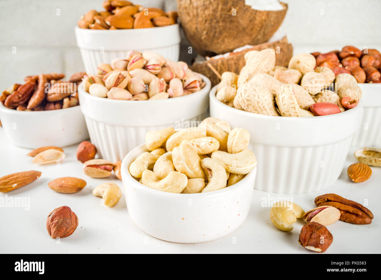 Verschiedene Arten von Nüssen - Walnüsse, Pekannüsse, Erdnüsse, Haselnüsse, Mandeln, Kokos, Cashews, in Schalen, auf einem weißen Marmor Tabelle Ansicht von oben Stockfoto