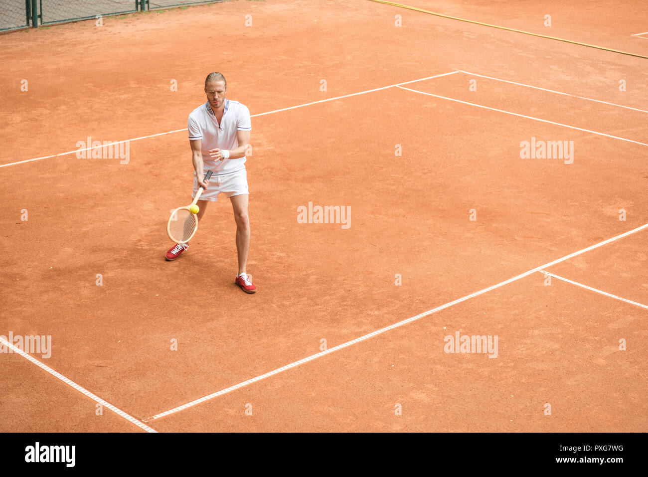 Altmodische tennis player Training mit hölzernen Schläger und Ball auf braun Hof Stockfoto