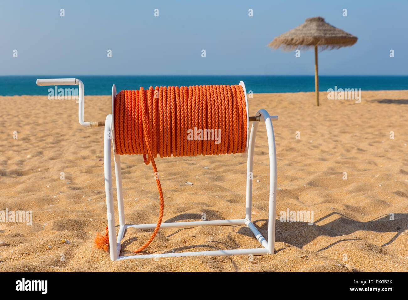 Haspel mit orange rescue Seil am Strand mit Sonnenschirm und Meer Stockfoto Haspel mit orange rescue Seil am Strand mit Sonnenschirm und Meer Stockfoto
