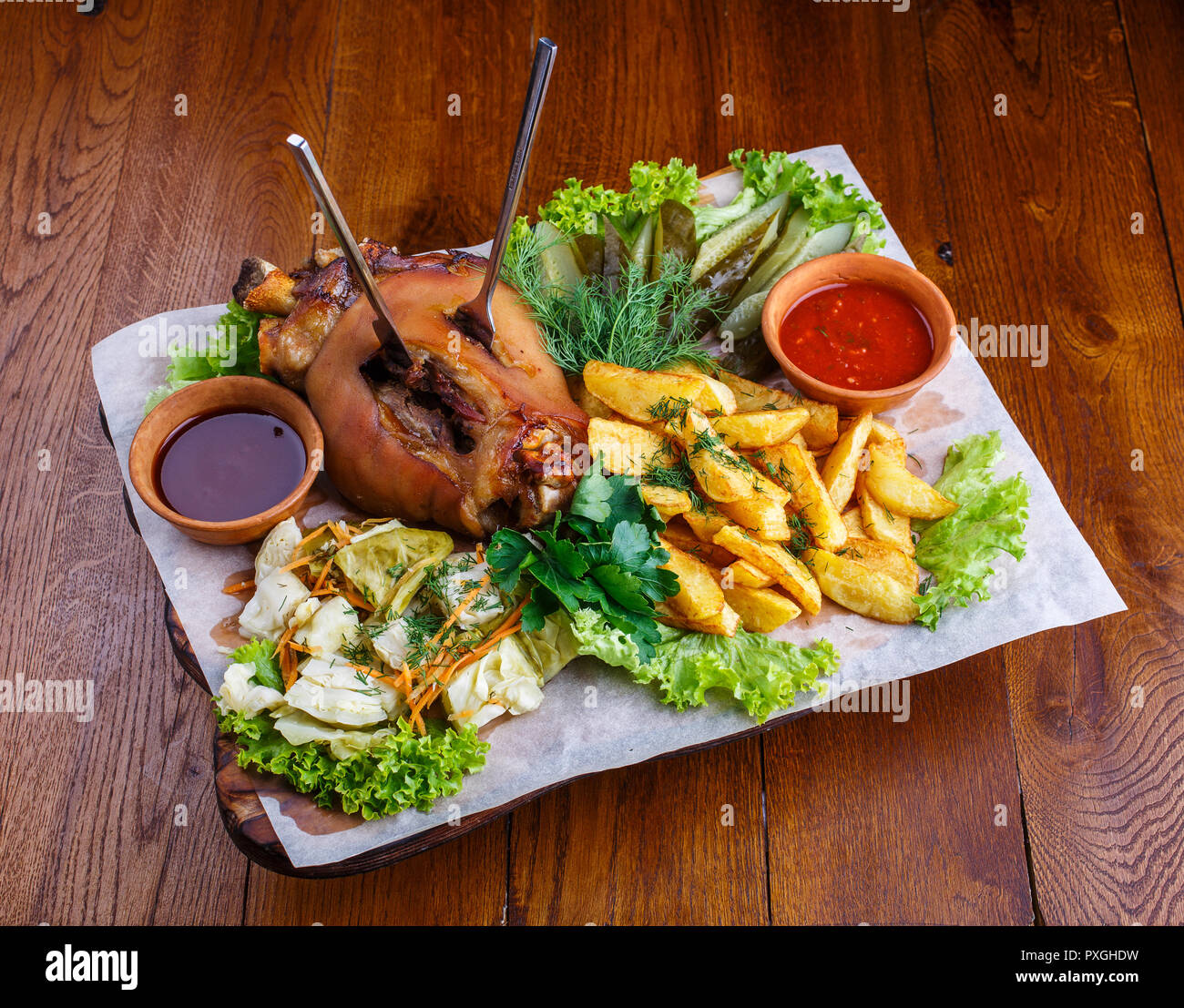 Moked Schweinekeule mit Kartoffeln, eingelegte Gurken, Kohl, Petersilie, Salat, Dill und roter Soße. Stockfoto