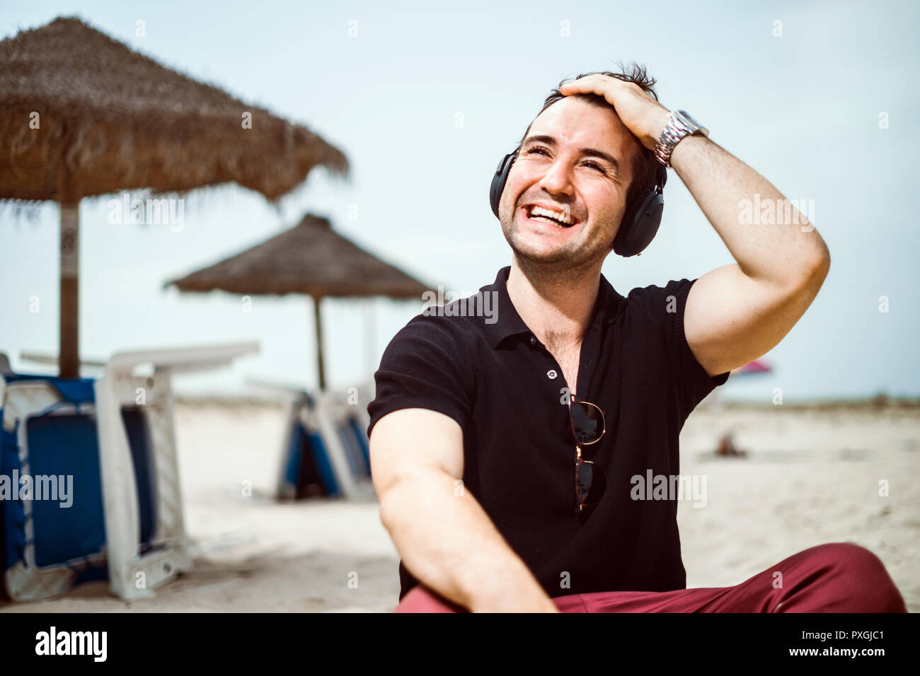 Modische Mann mit Lust auf Brille und Kopfhörer sitzen am Strand Stockfoto