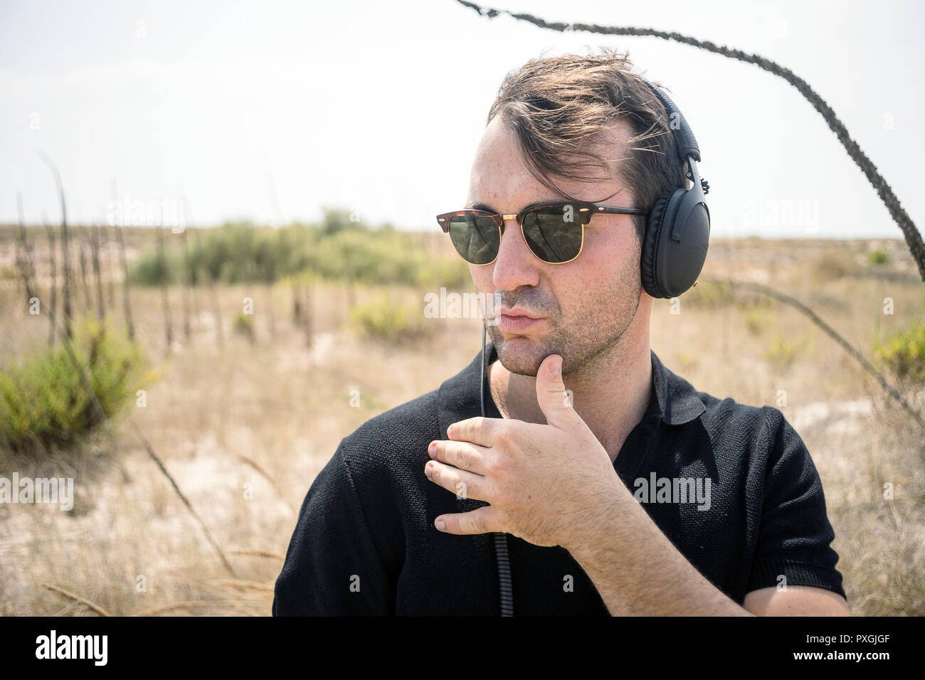 Modische Mann, ausgefallene Sonnenbrille und Kopfhörer in der Wüste Stockfoto