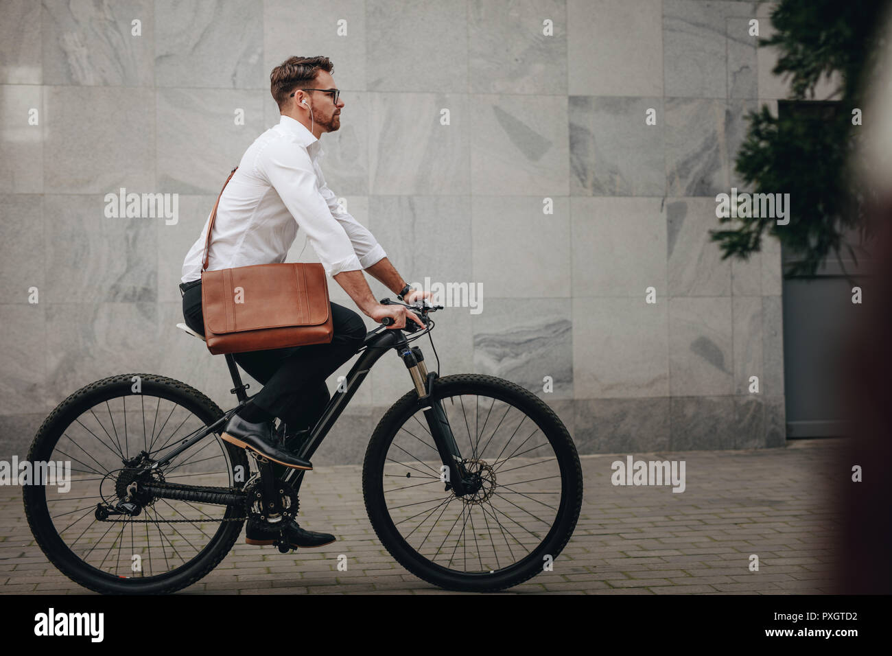 Seitliche Sicht auf ein Mann, der ein Büro Tasche mit dem Fahrrad. Unternehmer gehen zu Office auf ein Fahrrad, um Musik zu hören. Stockfoto