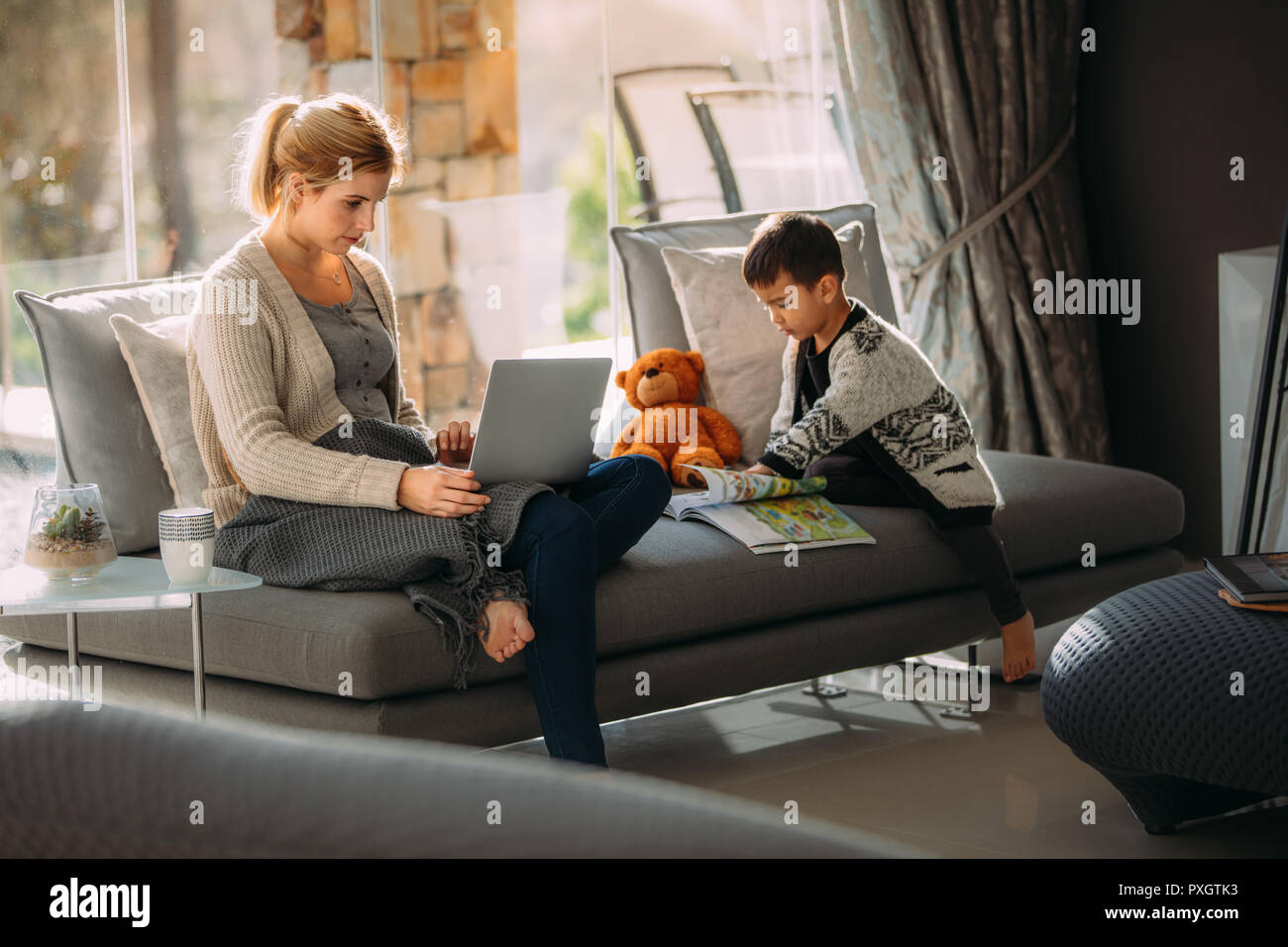 Frau Arbeiten am Laptop mit ihrem Sohn das Lesen ein Bilderbuch. Mutter arbeitet, die auf Notebook- und kleinen Jungen mit einem Bilderbuch zu Hause. Stockfoto
