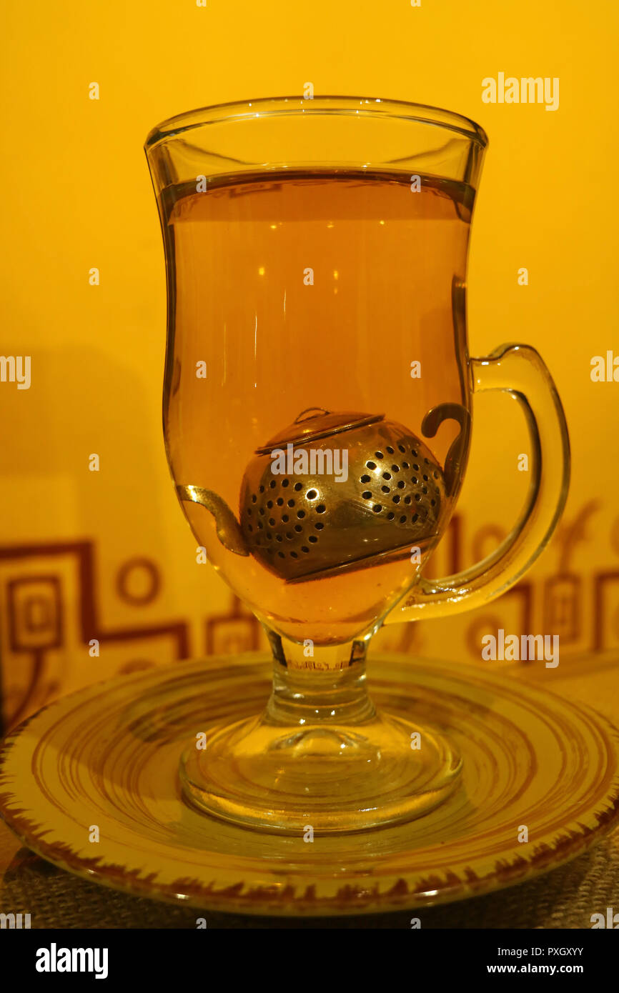 Heißen Kamillentee in transparenten Tee Tasse mit niedlichen Tea Leaf Filter vor der gelben wand serviert. Stockfoto