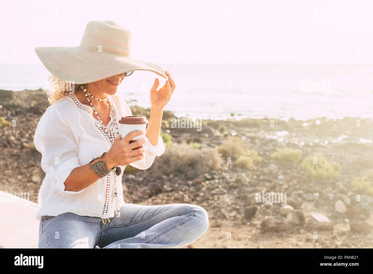 Ferien, Urlaub, Reisen und Menschen Konzept - lächelnde Frau, die in der Sun hat am Strand auf das Meer und die weißen Himmel Hintergrund. Kaffeebecher und glückliche Frau Stockfoto Ferien, Urlaub, Reisen und Menschen Konzept - lächelnde Frau, die in der Sun hat am Strand auf das Meer und die weißen Himmel Hintergrund. Kaffeebecher und glückliche Frau Stockfoto