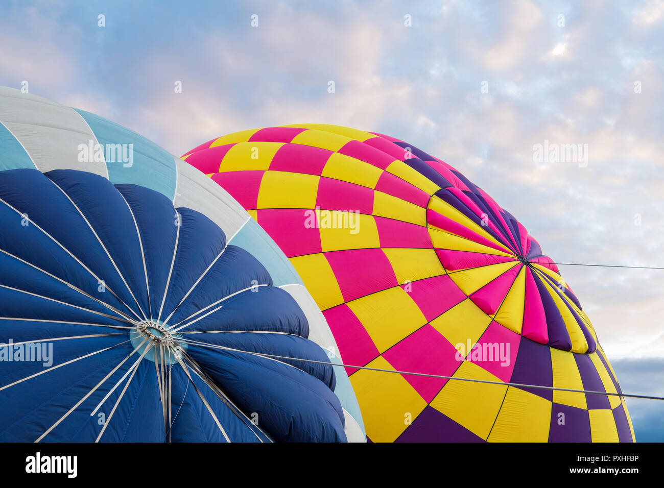 Bunte Heißluftballons in lebendigen Farben Blau, Lila, Rosa, Gelb und unter einem schönen Himmel am frühen Morgen bei Sonnenaufgang aufgepumpt werden Stockfoto