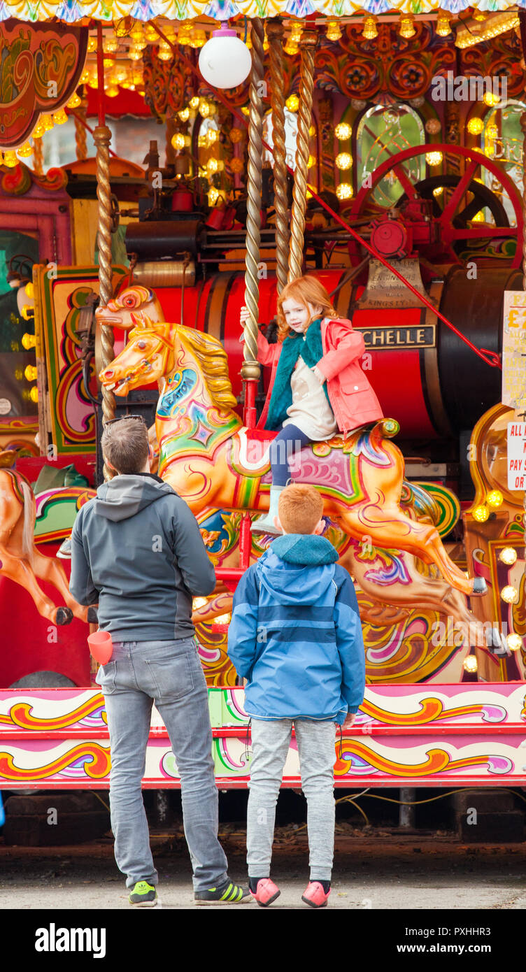 Familie Mutter und Vater, Kind auf der hobby horse auf der Kirmes Karussell Karussell in Tatton Park Cheshire England Großbritannien Stockfoto