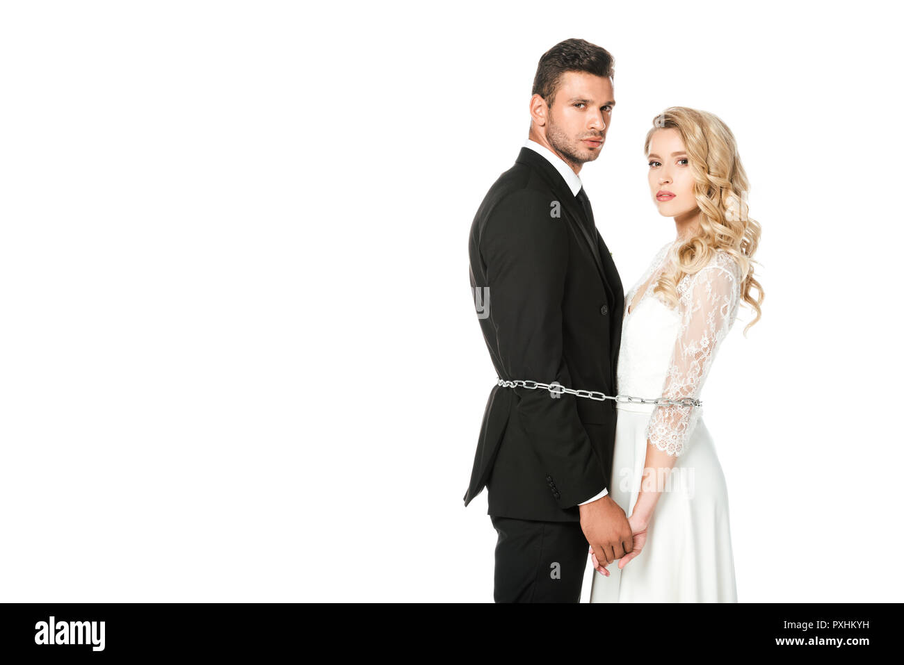 Ernsthafte junge Brautpaare mit Ketten gebunden und mit Blick auf die Kamera isoliert auf weißem Stockfoto