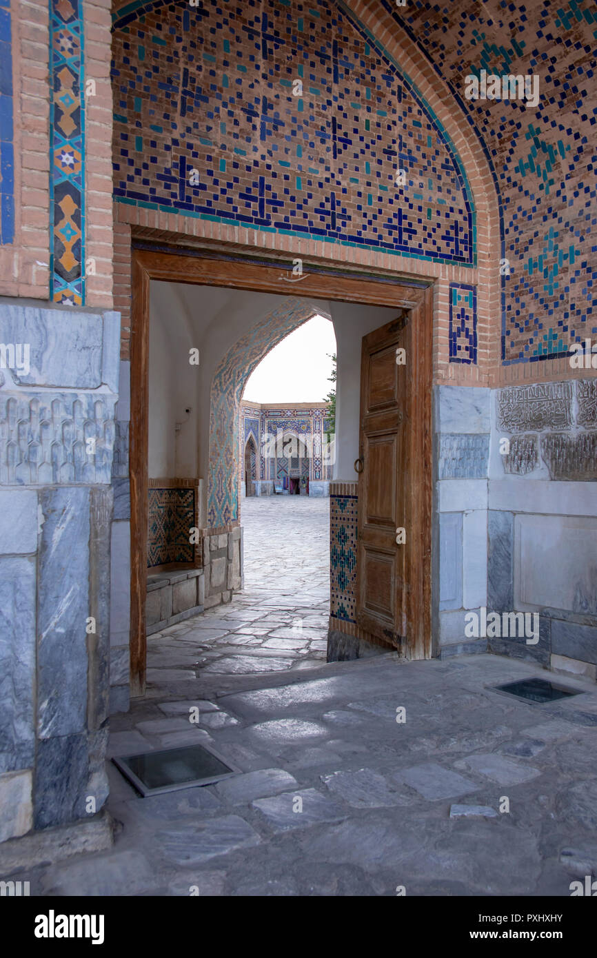 Cobblestone Eingang unter dem mosaischen Torbogen zum Innenhof der Medrese an der Registan in Samarkand, Usbekistan. Stockfoto