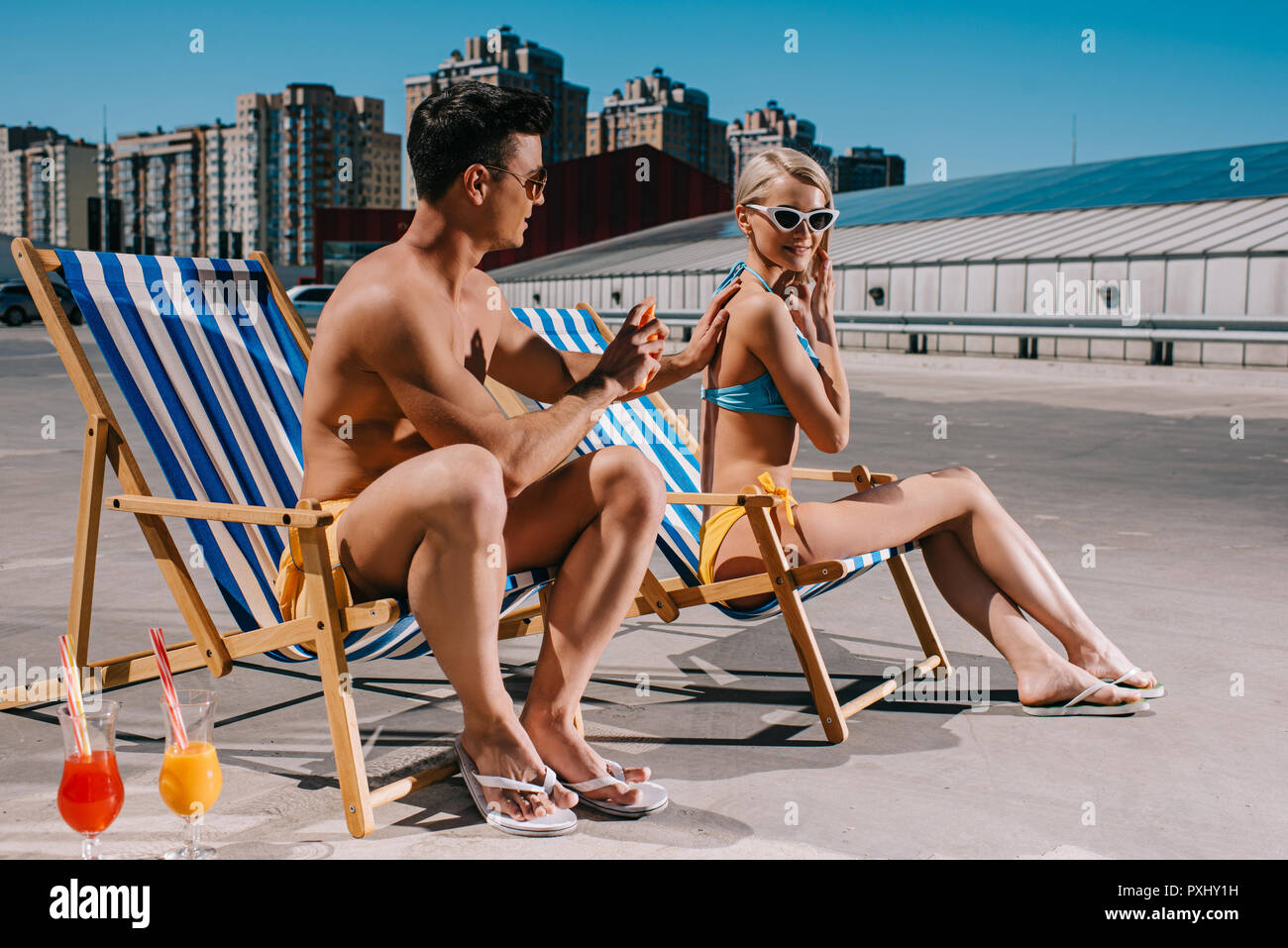 Junger Mann mit Sonnencreme auf Freundinnen wieder auf Parkplatz Stockfoto