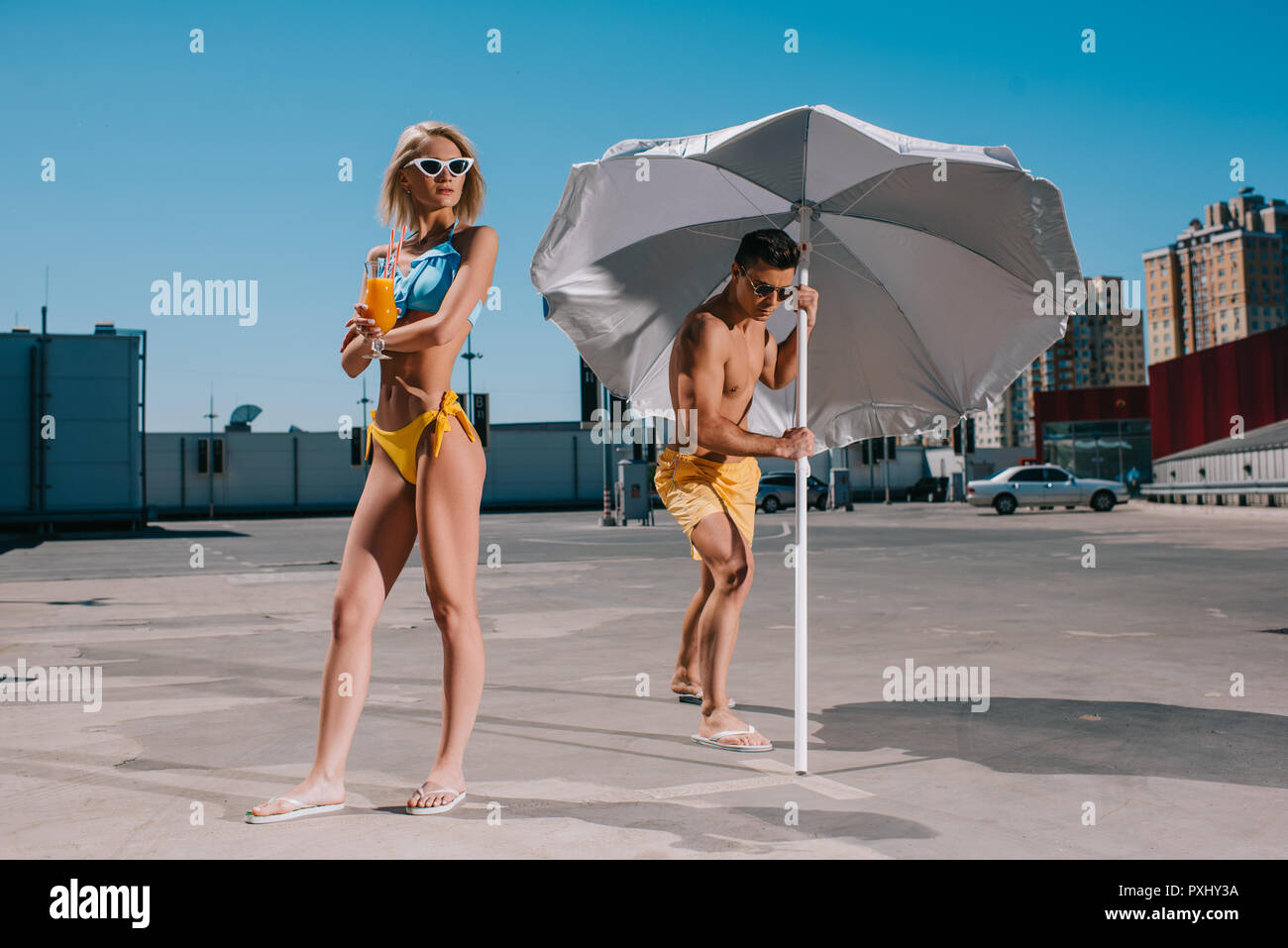 Junges attraktives Paar mit Sonnenschirm in Badebekleidung Gerben auf Parkplatz Stockfoto
