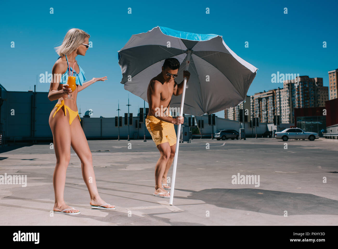 Junges Paar mit Sonnenschirm in Badebekleidung Gerben auf Parkplatz Stockfoto