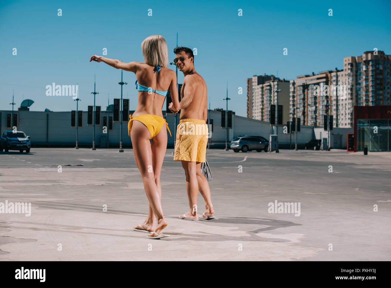 Ansicht der Rückseite des jungen attraktiven Paar in Bikini und Badeshorts irgendwo hin auf Parkplatz Stockfoto