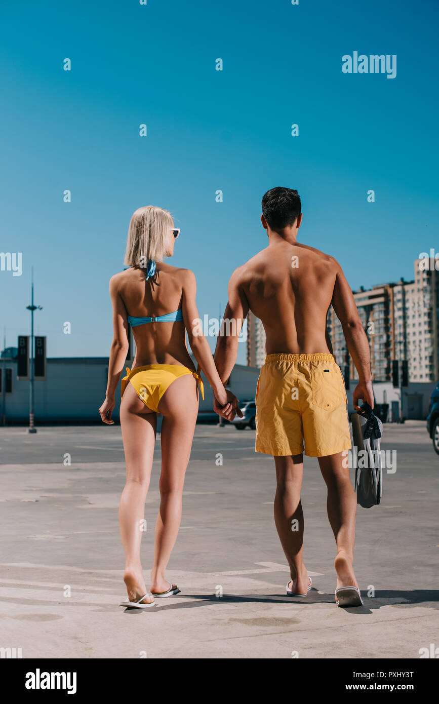 Ansicht der Rückseite des jungen attraktiven Paar in Bikini und Badeshorts mit Flossen auf dem Parkplatz Stockfoto
