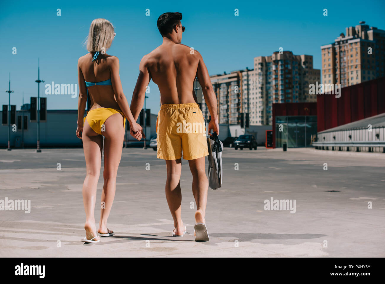 Ansicht der Rückseite des jungen Paares im Bikini und Badeshorts mit Flossen auf dem Parkplatz Stockfoto