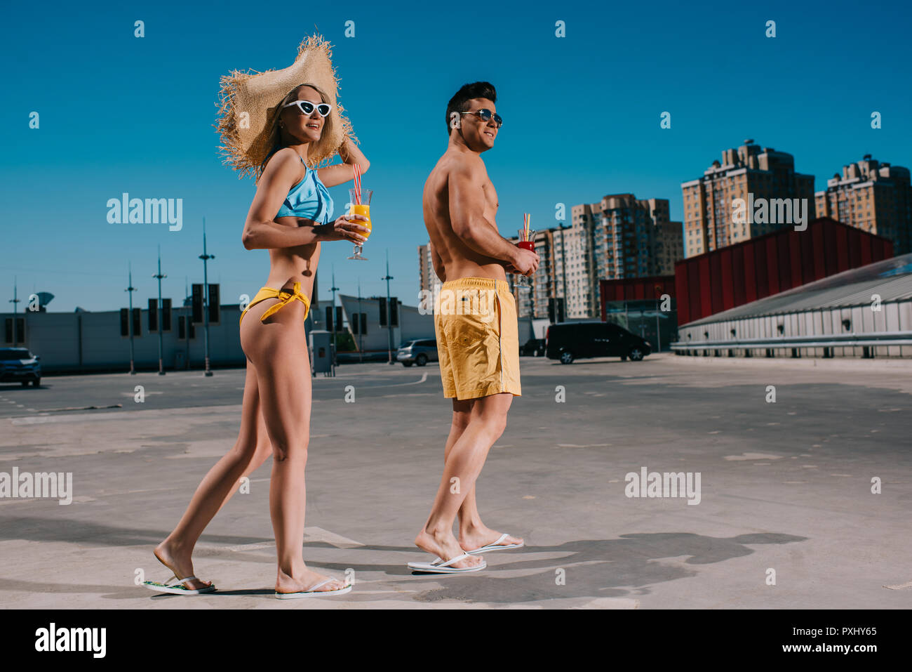 Junge glückliches Paar in Badebekleidung mit erfrischenden Cocktails stehen auf Parkplatz Stockfoto