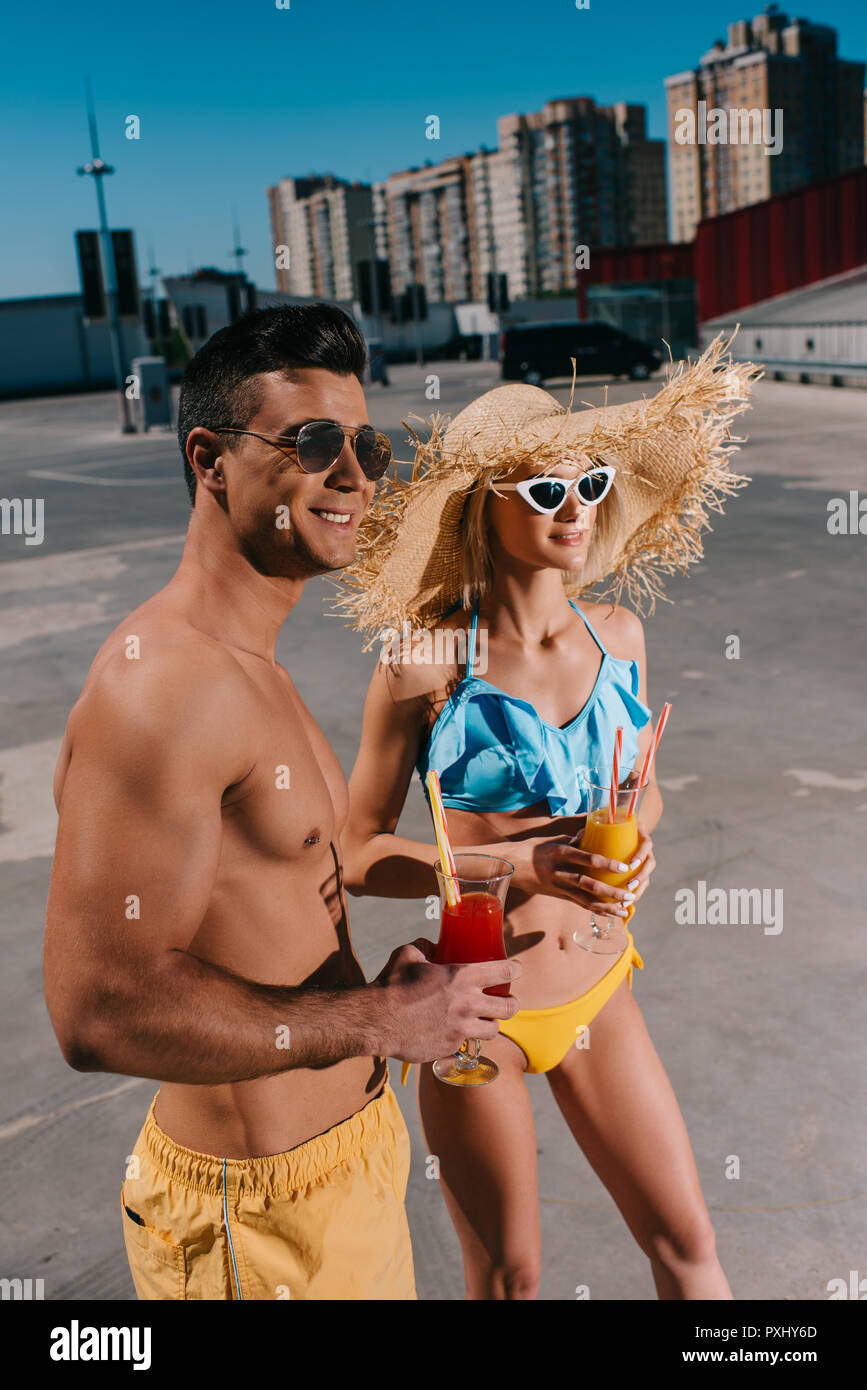 Gerne attraktive Paare in Badebekleidung mit erfrischenden Cocktails stehen auf Parkplatz Stockfoto