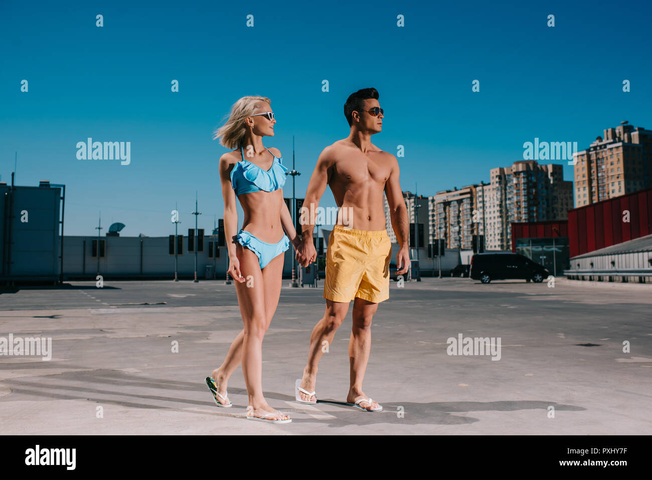 Attraktive junge Paar in Strand Kleidung halten sich an den Händen und laufen auf Parkplatz Stockfoto
