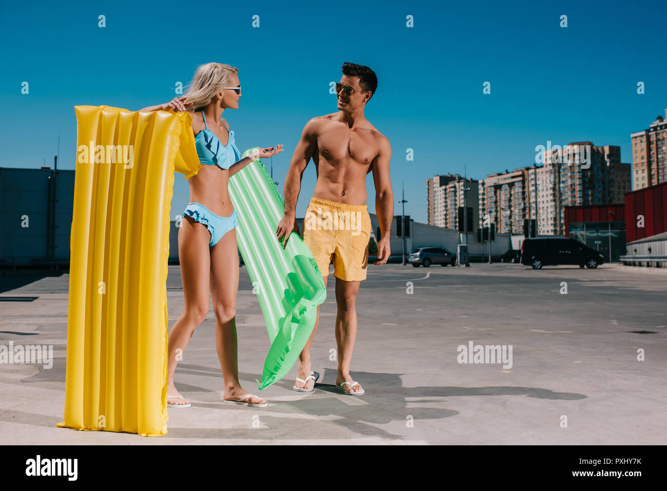 Attraktive junge Paar in Strand Kleidung mit aufblasbare Betten auf Parkplatz Stockfoto