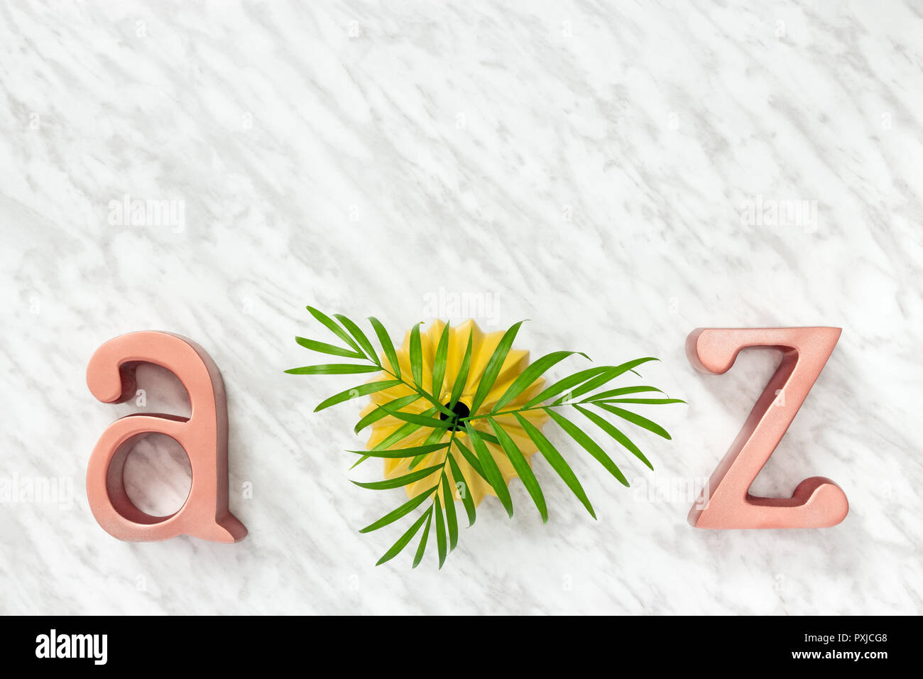 Metall Buchstaben A und Z und grünen Palmen Blätter in einem gelben Keramik Vase, auf Marmor Hintergrund. Stockfoto