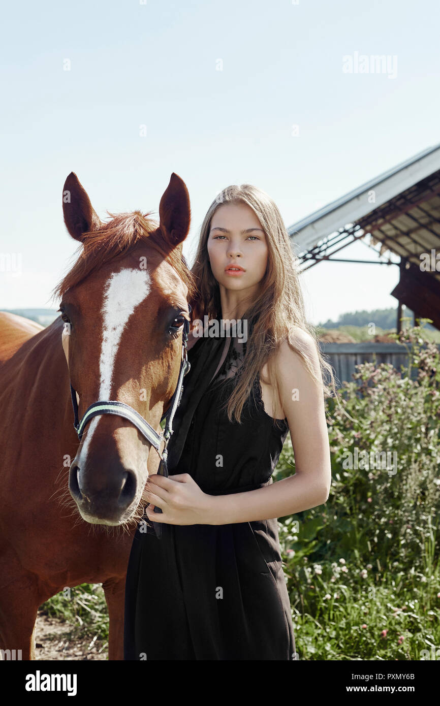 Mädchen Reiter steht neben dem Pferd in das Feld ein. Mode Porträt einer  Frau und die Stuten sind Pferde im Dorf im Gras. Blonde Frau holdi  Stockfotografie - Alamy