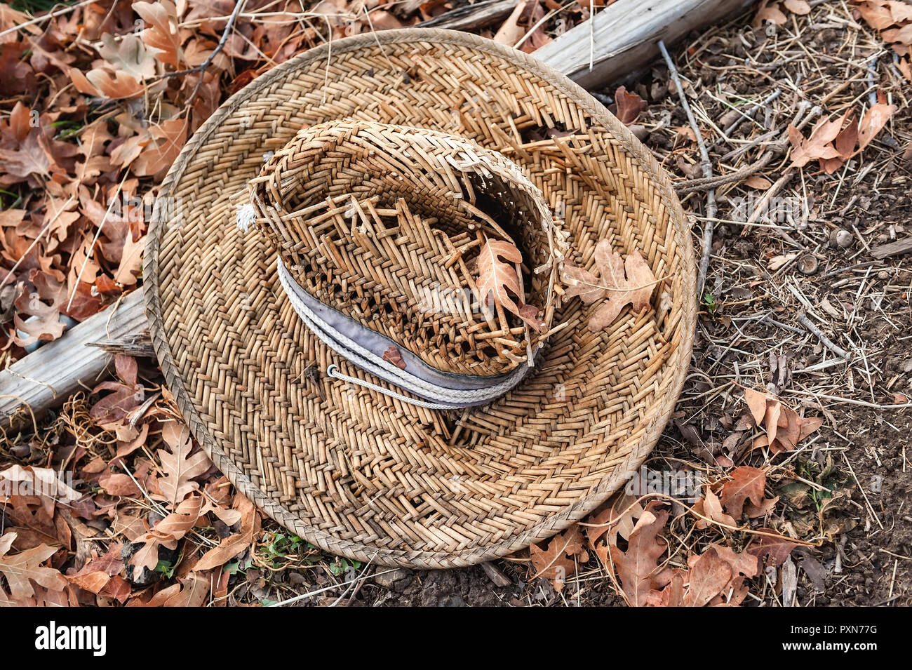 Eine alte gewebtem Stroh Hut auf einem Bett von braune Blätter im Herbst. Stockfoto