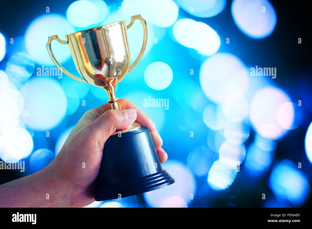 Sieger halten Trophäe mit Bokeh blaues Licht leuchtenden Hintergrund Stockfoto