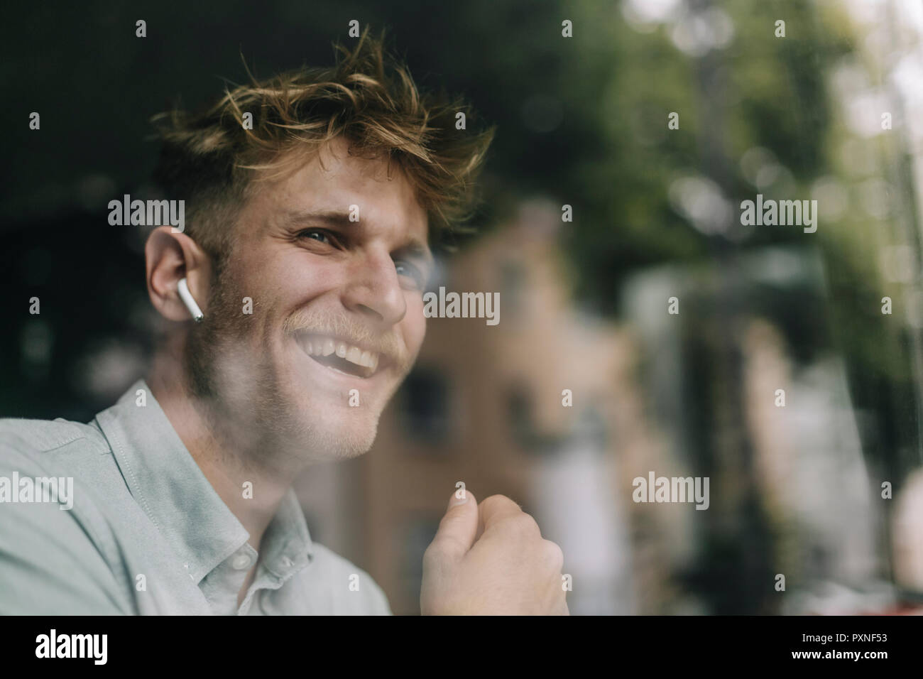 Junge Mann am Fenster, mit Ohrhörer, Lachen Stockfoto