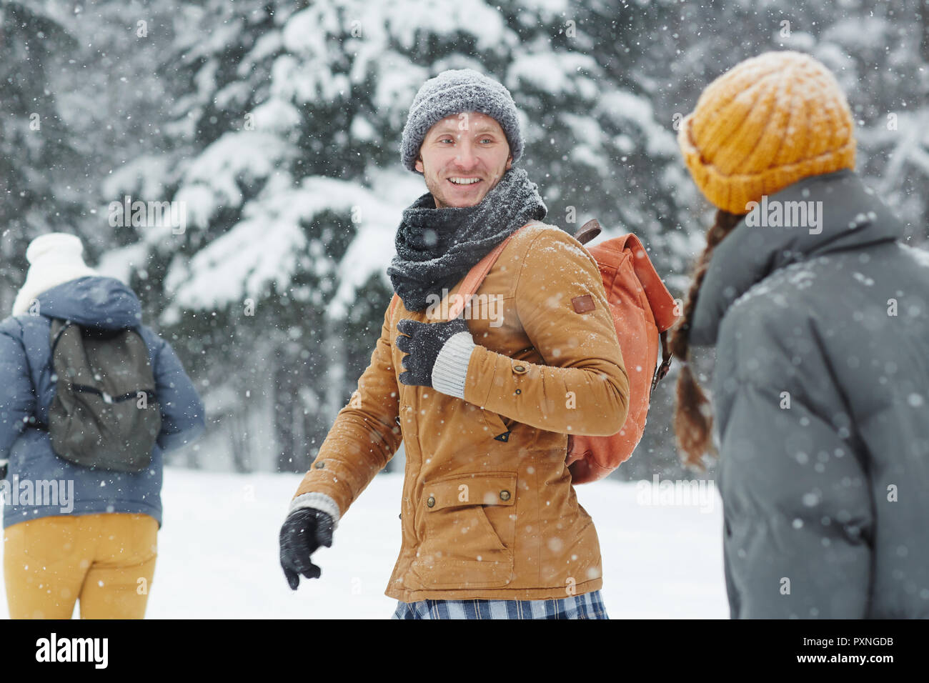 Lächelnd hübscher junger Wanderer in Hut und Schal zurück an Freund zu sprechen, während Sie zu Fuß in der Linie im Winter Wanderung Stockfoto