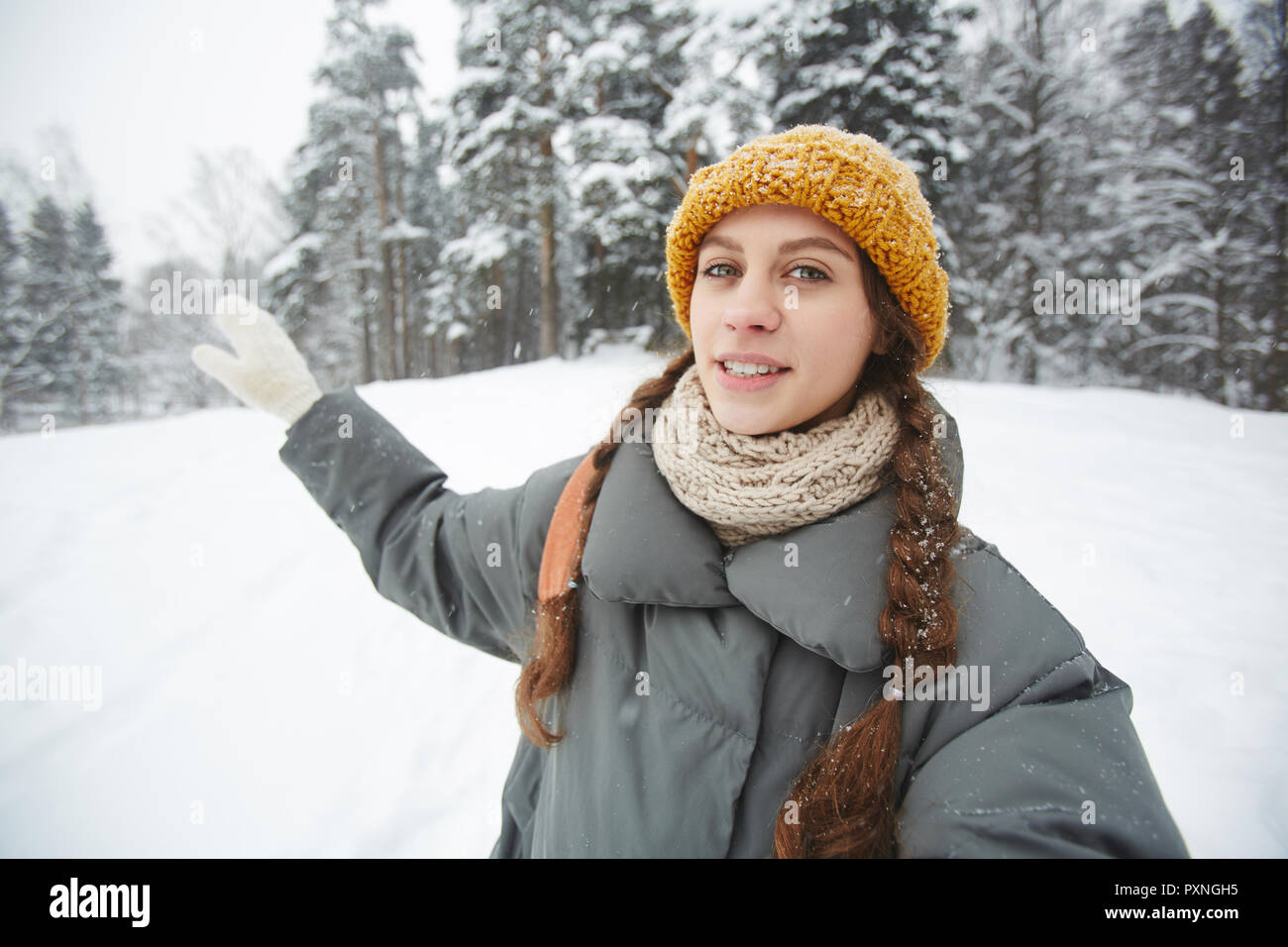 Lächelnd Inhalt junge weibliche Travel Blogger auf gestrickte Mütze und Schal Gestik, die Hand, während Sie mit Wald und die Tour im Winter Wald, Sie lookin Stockfoto