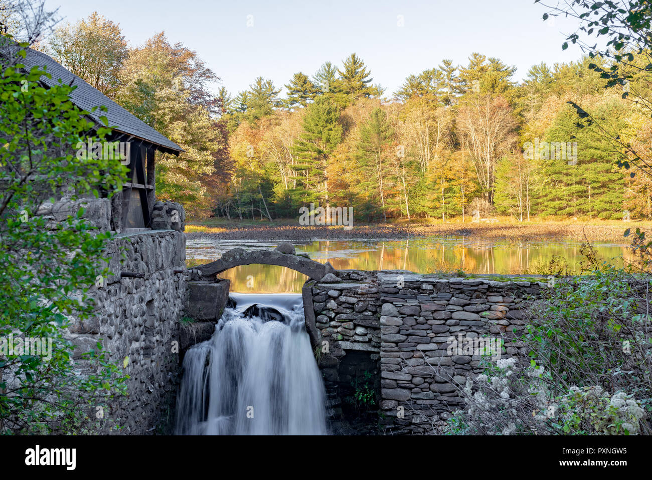 Steinmauer und Gebäude mit Wasserfall und Bäume im Herbst am See in Upstate New York wider. Stockfoto