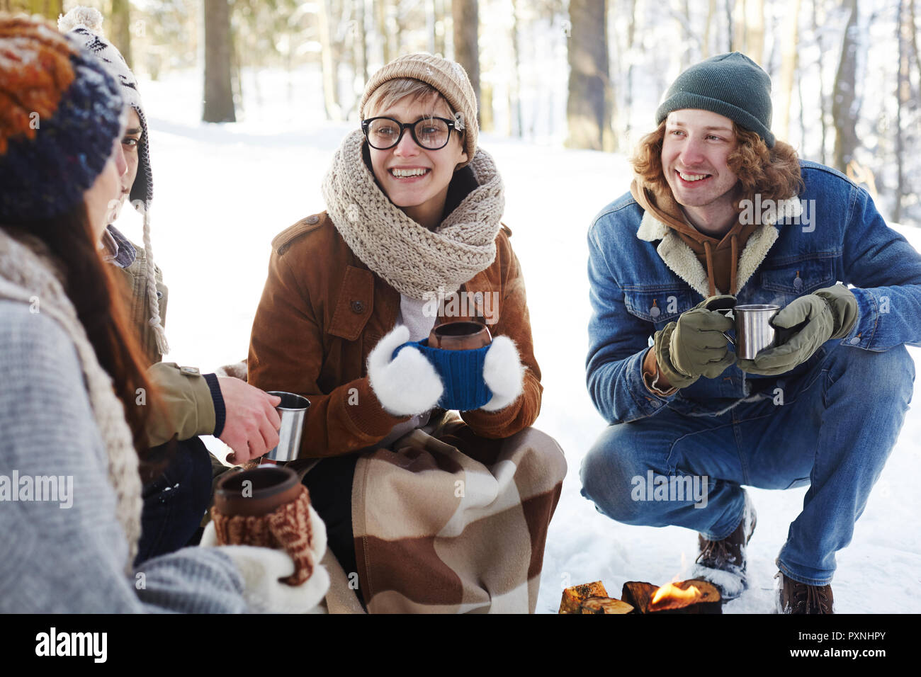 Portrait von glücklichen jungen Menschen Camping im Winter Wald im Kreis um das Feuer sitzen und plaudern, während Sie cups Stockfoto