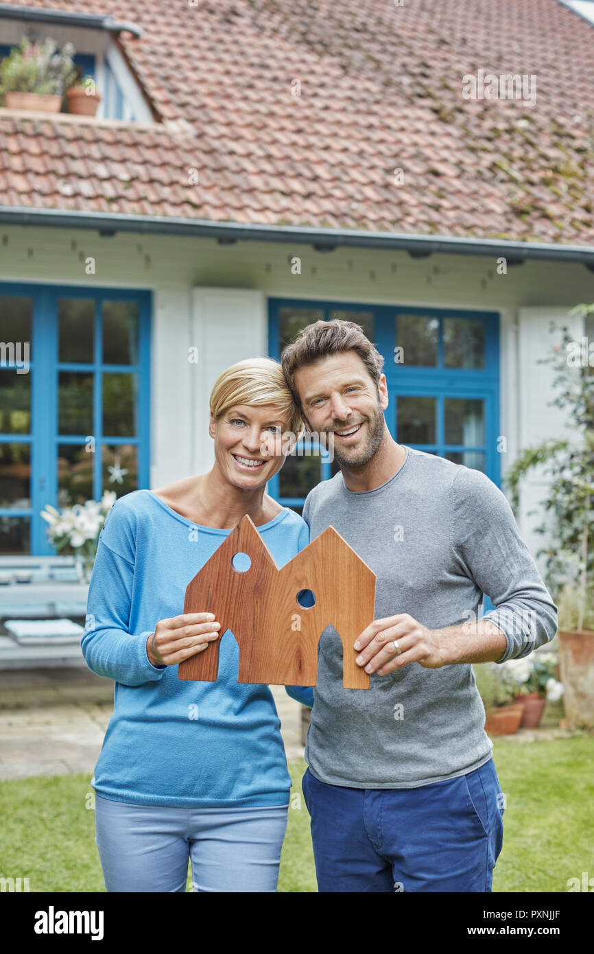 Portrait von lächelnden Paar steht vor ihrem Haus holding Haus Modell Stockfoto