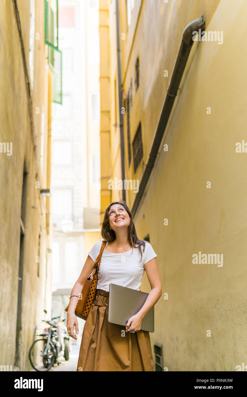 Lächelnde Frau wandern in einer Gasse mit Laptop Stockfoto