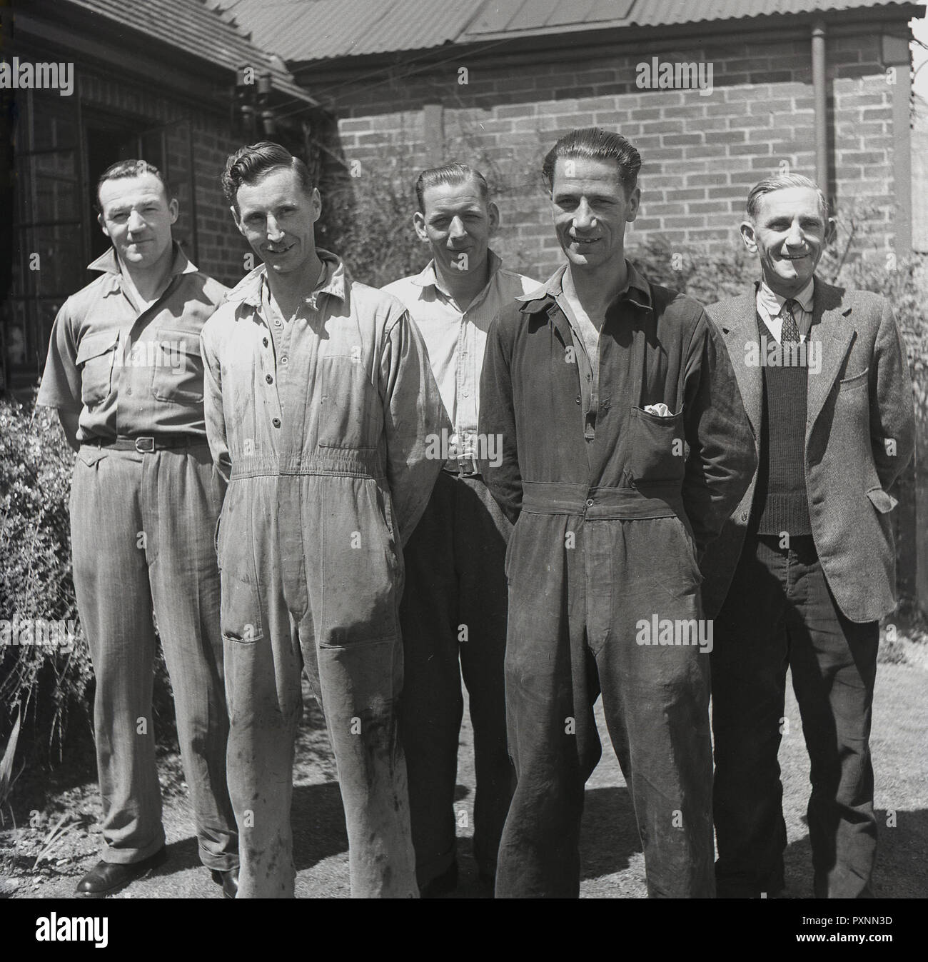 1950 s, historischen, einer Gruppe von reifen Fabrikarbeiter in Overalls und das Personal der Büros in ziviler Kleidung zusammen für ein Bild außerhalb, England, UK. Stockfoto