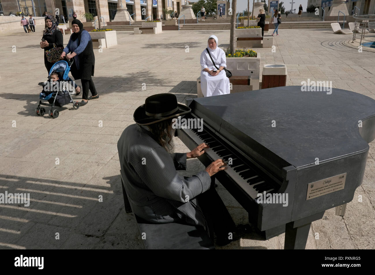 Palästinensische Frauen und einer katholischen Nonne in einem ultra-orthodoxe Juden suchen Spielen ein Klavier aus Beton durch die Kadenz in Safra Square auf der Jaffa Road West Jerusalem Israel Stockfoto