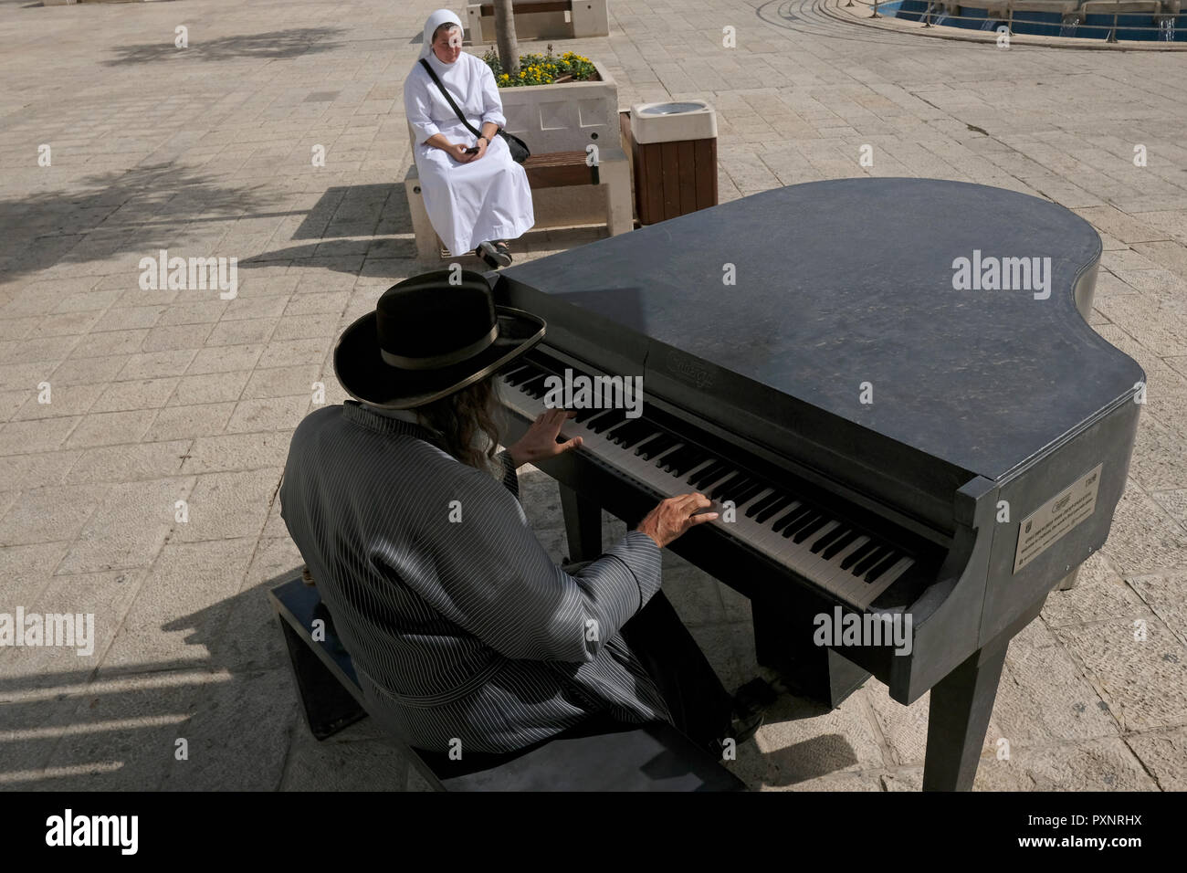 Eine katholische Nonne sitzt neben einer Ultra-orthodoxen Juden spielen ein Klavier aus Beton durch die Kadenz in Safra Square auf der Jaffa Road West Jerusalem Israel Stockfoto