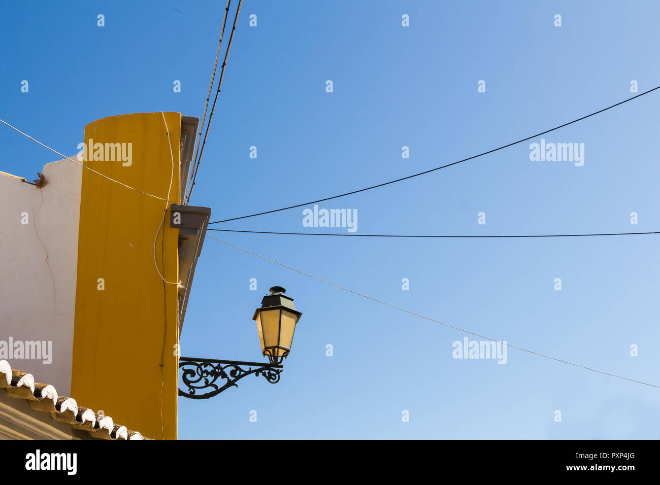 Ecke eines Gebäudes mit einer Laterne. Die Farbe der Fassade ein Glas der Lampe. Strom Kabel in jeder Richtung. Blue Sky. Faro, Portugal Stockfoto