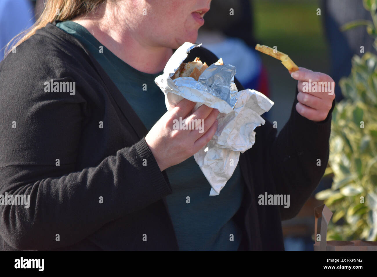 Fettleibigkeit UK, Fast-Food-Outlets verantwortlich gemacht. Fast Food wird durch eine übergewichtige Dame im Britischen Straße sitzend gegessen. Okt 2018 Stockfoto