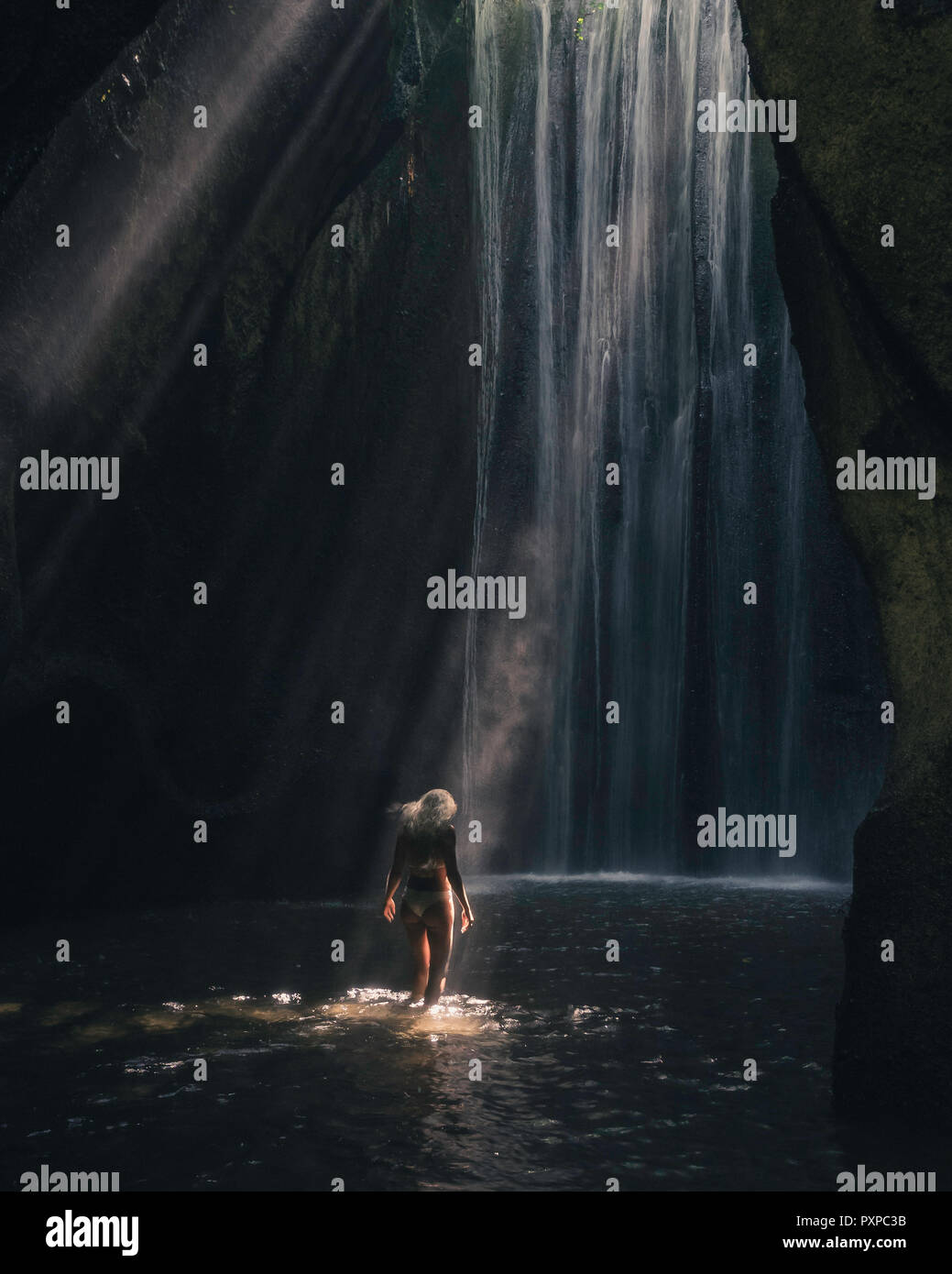 Frauen in den Fluss vor der Wasserfall, die von Lichtstrahl beleuchtet Stockfoto